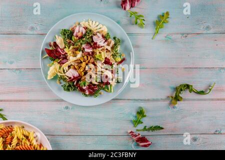 Frischer grüner Salat mit Rucola, Blumenkohl, Grünkohl und Pistazien auf Holzgrund. Vegetarische Gerichte. Stockfoto