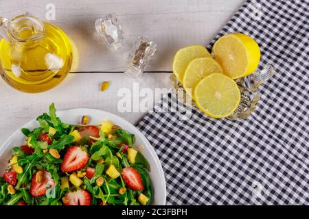 Frischer saftiger Salat mit Rucola, Erdbeeren Pistazien. Gesunder Salat neben Zitrone und Olivenöl. Stockfoto