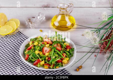 Erdbeersalat mit Rucola, Mango und Pistazien mit Zitrone und Olivenöl auf Holztisch mit Blumen. Stockfoto