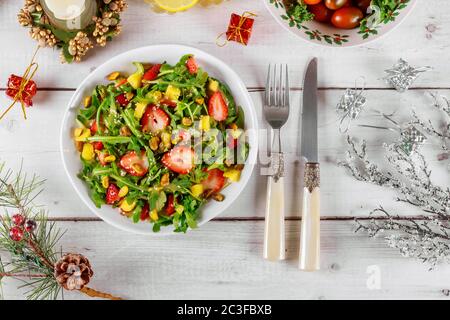 Salat mit Rucola, Erdbeeren und Ananas mit weihnachtlicher Dekoration auf weißem Holztisch. Stockfoto