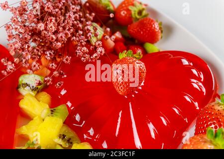 Erdbeerherz-Gelatine mit Früchten und Blumen am Valentinstag oder Hochzeit. Stockfoto