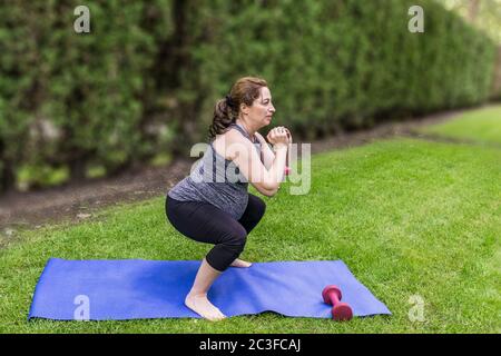 Gesunde schwangere Frau, die Yoga mit Hanteln in der Natur im Freien macht. Stockfoto