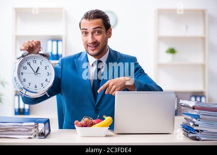 Junger männlicher Mitarbeiter beim Frühstück am Arbeitsplatz Stockfoto