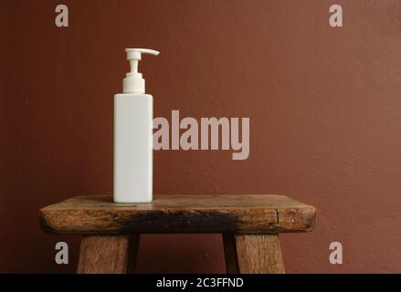 Closeup weiße Sprühflasche auf Vintage Holzstuhl gegen braun bemalte Wand platziert Stockfoto