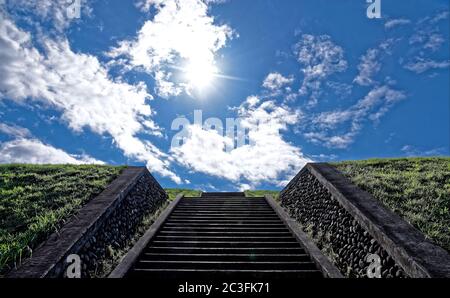 Blick auf einen tiefblauen Himmel und Betontreppen, die an einem sonnigen Tag im Spätsommer auf einen grasbewachsenen Hügel führen Stockfoto