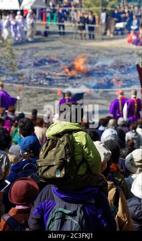 Ein kleiner Junge, der auf den Schultern eines Erwachsenen sitzt und ein traditionelles Feuerwanderfestival in der Nähe des Mount Takao im Westen Tokios beobachtet Stockfoto