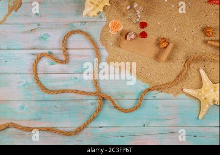 Herz aus Seil an der Küste mit Muscheln. Valentinstag-Konzept. Papyrus aus der Glasflasche mit Kork. Stockfoto