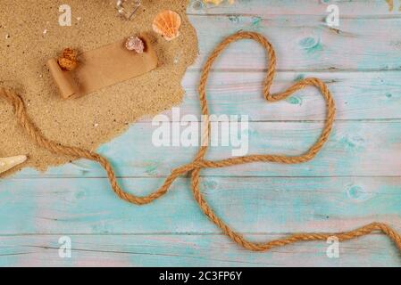 Herz aus Seil an der Küste mit Muscheln. Valentinstag-Konzept. Papyrus aus der Glasflasche mit Kork. Stockfoto