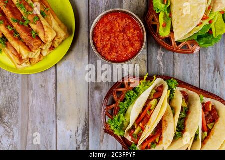 Taquitos, weiche Tortillas und milde Salsa auf Holztisch. Stockfoto