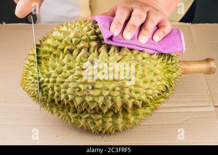 Frau schneidet eine Durian Frucht auf dem Holztisch, indem sie ein Messer aus der Nähe benutzt. Durian ist die beliebte Frucht in Thailand. Stockfoto