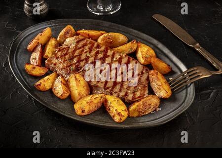 Gegrilltes Rindersteak mit gebackenen Kartoffelkeilen auf schwarzem Hintergrund Stockfoto