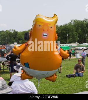 Washington, D.C., USA. Juni 2019. Der Heliumballon des Protesters, der eine Cartoon-Version von Präsident Donald J. Trump als Baby in Windeln mit einem russischen Hammer und Sichelemblem auf seiner Windelnadel darstellt, Und ein Putins Herz-Tattoo und die Trikolore der russischen Flagge auf seinen Armen schweben über den mit Krempen bemalten Hüten auf den Köpfen der Teilnehmer beim Nationalmarsch, um zu entheben; ein Mann mit einer Kamera um den Hals im Hintergrund. Die von der Gruppe People Demand Action organisierte Demonstration auf dem Washington Monument Grounds forderte den Kongress der Vereinigten Staaten auf, ein Amtsenthebungsverfahren einzuleiten. Kay Howell/Alamy Stockfoto