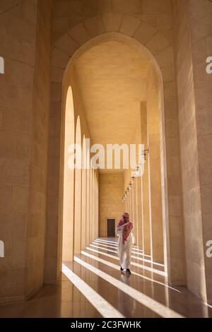 Manama / Bahrain - 10. Januar 2020: Muslimischer Mann in traditioneller muslimischer Kleidung und Kopftuch, der vor dem Sonnenuntergang mit schönem Licht in die Al-Fateh Moschee geht Stockfoto