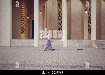 Manama / Bahrain - 10. Januar 2020: Muslimischer Mann in traditioneller muslimischer Kleidung und Kopftuch, der vor dem Sonnenuntergang mit schönem Licht in die Al-Fateh Moschee geht Stockfoto