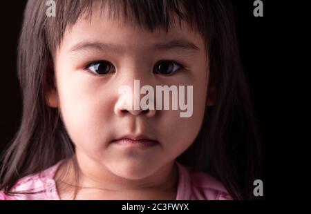 Portrait Gesicht von asiatischen kleinen Mädchen mit Vertrauen Ausdruck auf dunklem Hintergrund. Stockfoto