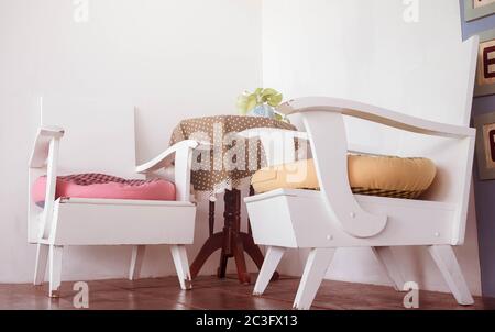 Weiße Holzstühle und Holztisch mit schönen farbigen Tischdecken und niedlichen kleinen Blumenvase in der Wohnecke im Café. Entspannungsecke Stockfoto