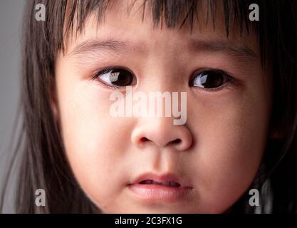 Portrait Gesicht von asiatischen kleinen Mädchen mit trauriger Ausdruck auf dunklem Hintergrund. Stockfoto