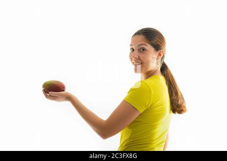 Seitenansicht einer glücklich aussehenden jungen Frau, die eine köstliche Mango auf einem hellen Hintergrund hält. Gesundes Essen und Lifestyle-Konzept. Stockfoto