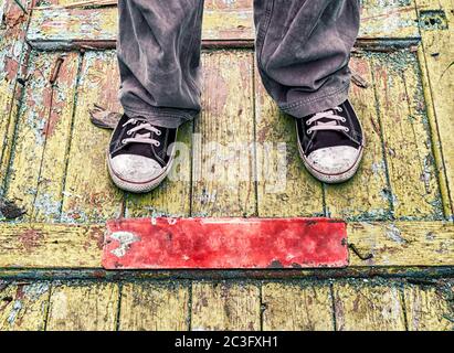 Beine eines Mannes in alten schmutzigen Schuhen auf einem gelben Holzboden Stockfoto