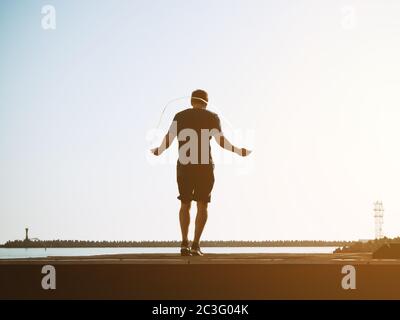 Junger Mann in Shorts springt an einem sonnigen Tag am hintergrundigen Himmel auf einem Seil. Künstlerische Wirkung. Verschwommenes Bild Stockfoto