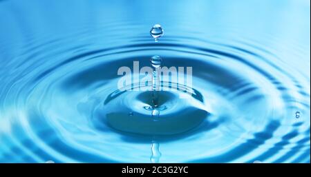 Wassertropfen, der in Wasser fällt und so eine perfekte konzentrische Kreisfläche darstellt. Abstrakter blauer Hintergrund. Stockfoto