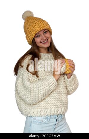 Schöne glückliche Mädchen hält in ihren Händen zwei Garnkugeln und trägt einen Pullover und Mütze, gestrickt dicken Faden. Handgefertigte Winterkleidung. Isoliert. Stockfoto