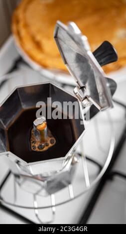 Kaffee in Moka Topf mit Pfannkuchen im Hintergrund vorbereiten. Kaffee zu Hause mit italienischen Wasserkocher aus Edelstahl Stockfoto