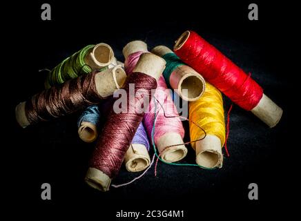 Stapel von gebrauchten bunten Spulen von Thread Schneiderei, auf schwarzem Hintergrund Stockfoto