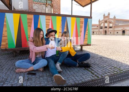 Zwei Mädchen sitzen auf dem Boden neben einem Mann in einem Hut lächelnd und feiern. Bunte und leuchtende Hintergrund mit Platz für Text Stockfoto