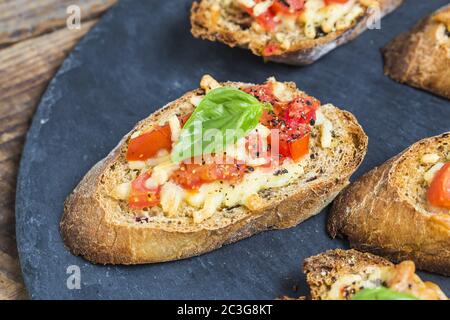 Italienische Bruschetta mit gerösteten Tomaten, Mozzarella-Käse und Kräutern auf ein Schneidebrett Stockfoto