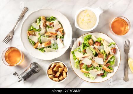 Caesar Salat mit der klassischen Sauce und Wein, von oben auf einem weißen Marmorgrund geschossen Stockfoto