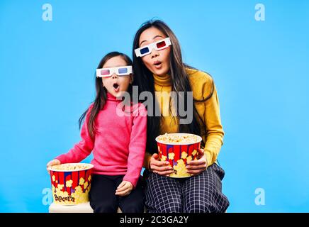 Überraschte Mutter und ihre kleine Tochter in 3D-Brille mit Popcorn Film über blauen Hintergrund Stockfoto