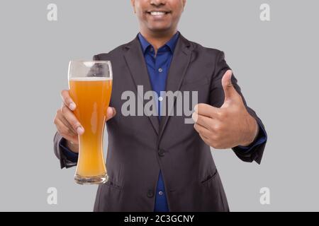 Geschäftsmann zeigt Bierglas und Daumen hoch. Indischer Geschäftsmann mit Bier in der Hand Nahaufnahme Stockfoto