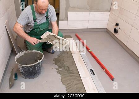 Ein Bauarbeiter schmiert den Boden der Keramikfliesen mit einer Metallkelle mit Spezialleim. Stockfoto