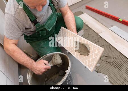 Ein Bauarbeiter schmiert den Boden der Keramikfliesen mit einer Metallkelle mit Spezialleim. Stockfoto