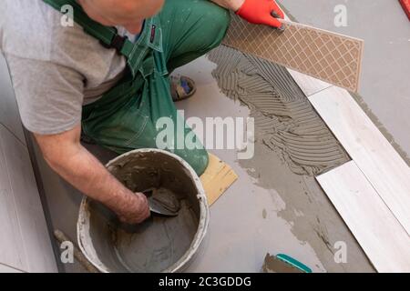 Ein Bauarbeiter schmiert den Boden der Keramikfliesen mit einer Metallkelle mit Spezialleim. Stockfoto