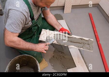 Ein Bauarbeiter schmiert den Boden der Keramikfliesen mit einer Metallkelle mit Spezialleim. Stockfoto