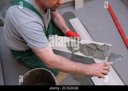 Ein Bauarbeiter schmiert den Boden der Keramikfliesen mit einer Metallkelle mit Spezialleim. Stockfoto