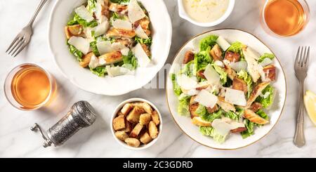 Caesar Salatpanorama mit klassischer Soße und Wein, aufgenommen von oben auf weißem Marmorgrund Stockfoto