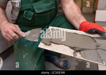 Ein Bauarbeiter schmiert den Boden der Keramikfliesen mit einer Metallkelle mit Spezialleim. Stockfoto