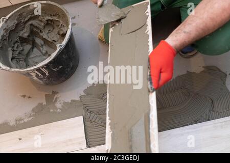 Ein Bauarbeiter schmiert den Boden der Keramikfliesen mit einer Metallkelle mit Spezialleim. Stockfoto