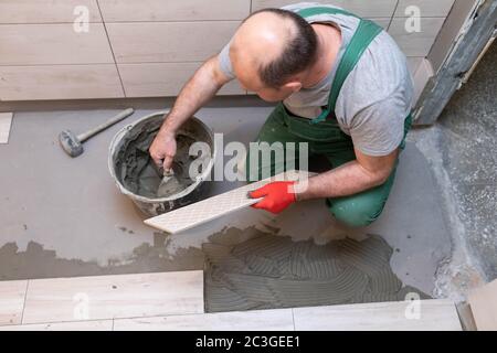 Ein Bauarbeiter schmiert den Boden der Keramikfliesen mit einer Metallkelle mit Spezialleim. Stockfoto