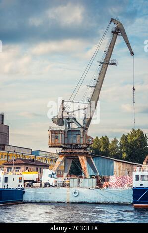 Ein rostiger Ladekran im Hafen in der Nähe von Lagerhäusern in St. Petersburg Stockfoto