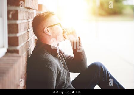 Einsamer depressiver Mann sitzt auf dem Boden gegen eine Wand Mit hellem Sonnenlicht im Hintergrund Stockfoto