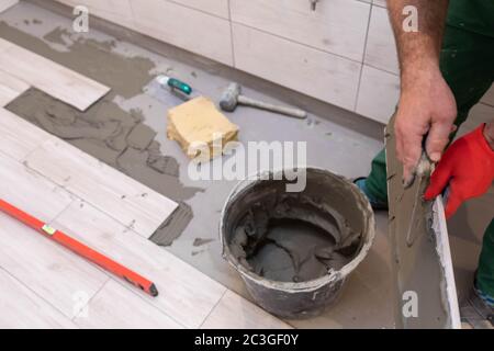 Ein Bauarbeiter schmiert den Boden der Keramikfliesen mit einer Metallkelle mit Spezialleim. Stockfoto