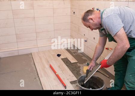 Ein Bauarbeiter schmiert den Boden der Keramikfliesen mit einer Metallkelle mit Spezialleim. Stockfoto