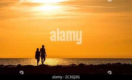 Silhouette von Menschen, die während der goldenen Stunde des Sonnenuntergangs auf dem Pier spazieren gehen und radeln Stockfoto