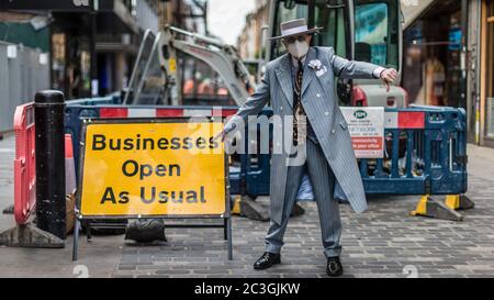 Ein gut gekleideter Mann in einer Maske steht bei einem "Businesses Open as usual"-Schild in Soho, als die Sperre in London gelockert wird. Stockfoto