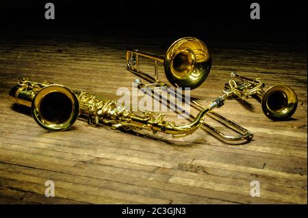 Gelbe Blas- und Blasinstrumente - Saxofon, Posaune, Trompete auf Holzbühne mit Hintergrundbeleuchtung Stockfoto