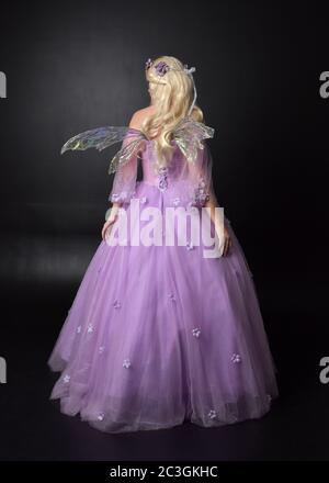 Portrait einer schönen blonden Fee trägt lila Fantasy-Kleid mit Flügeln. In voller Länge stehende Pose, isoliert vor einem Studio-Hintergrund. Stockfoto